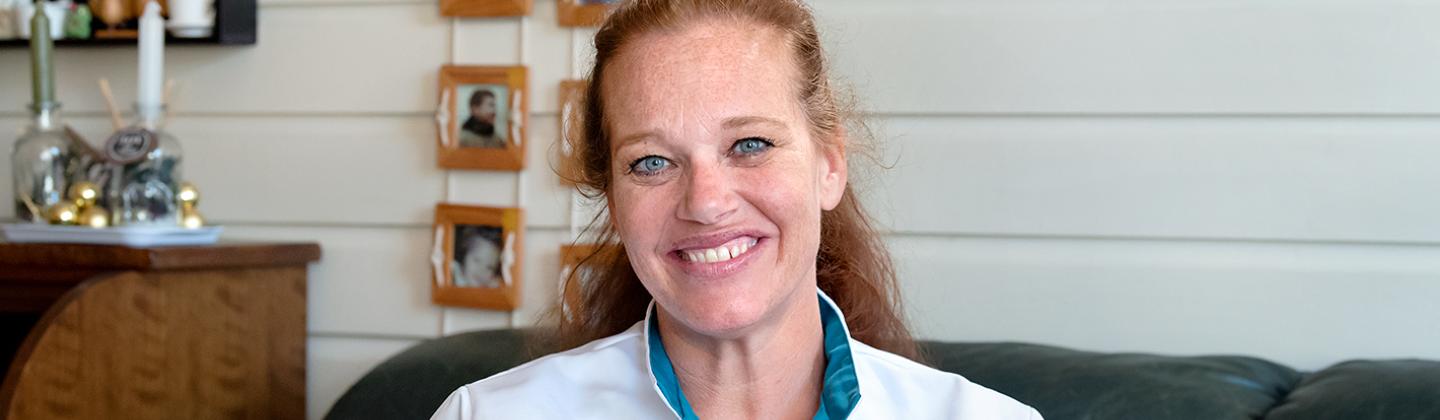 Medewerker van de Omring thuiszorg poseert voor de camera. Ze lacht en zit op de bank in de woonkamer van een cliënt.